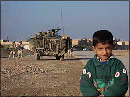 Taking a chance to be famous, a young Samarran poses for a photo, with the ever-present occupiers behind.